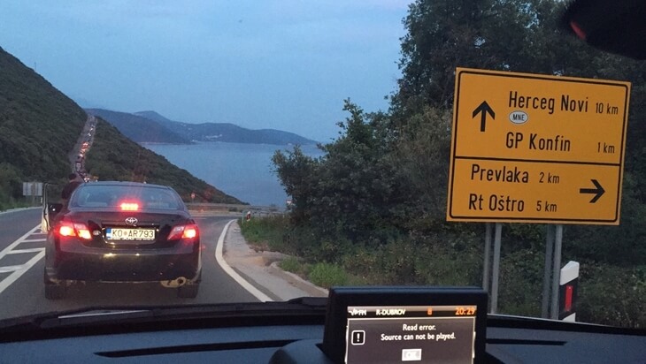 Montenegro-Croatia Border Crossing near Herceg Novi Cars waiting at twilight near road signs marking distances to Herceg Novi and Croatian border crossings at the Montenegro-Croatia border.