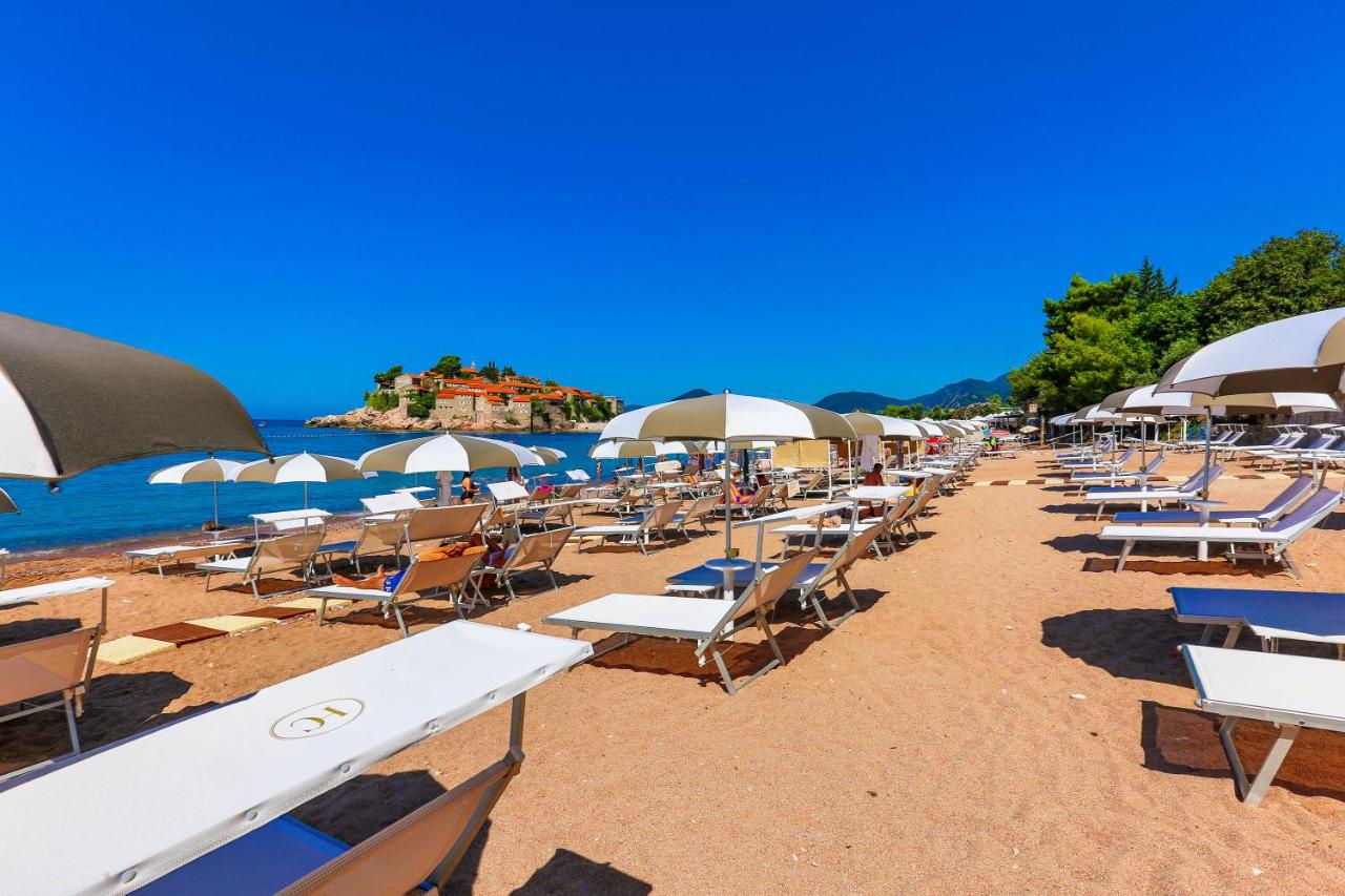 Relaxing Beachfront at Hotel California, Sveti Stefan Montenegro White sun loungers and umbrellas on a sandy beach, facing the iconic Sveti Stefan island, at Hotel California in Montenegro.
