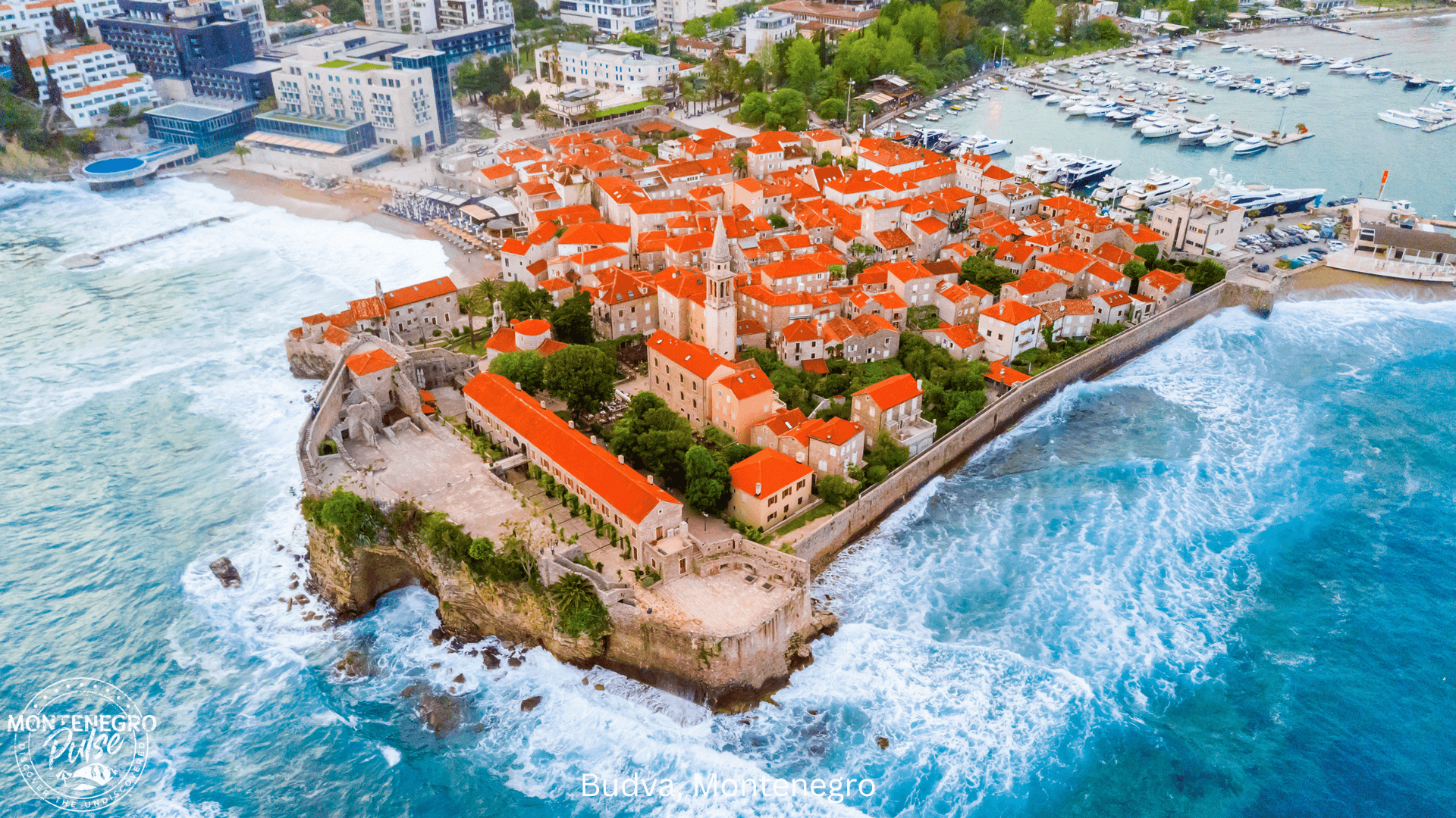 Aerial view of Budva's Old Town with red rooftops and the coastline along the Adriatic Sea, Montenegro.