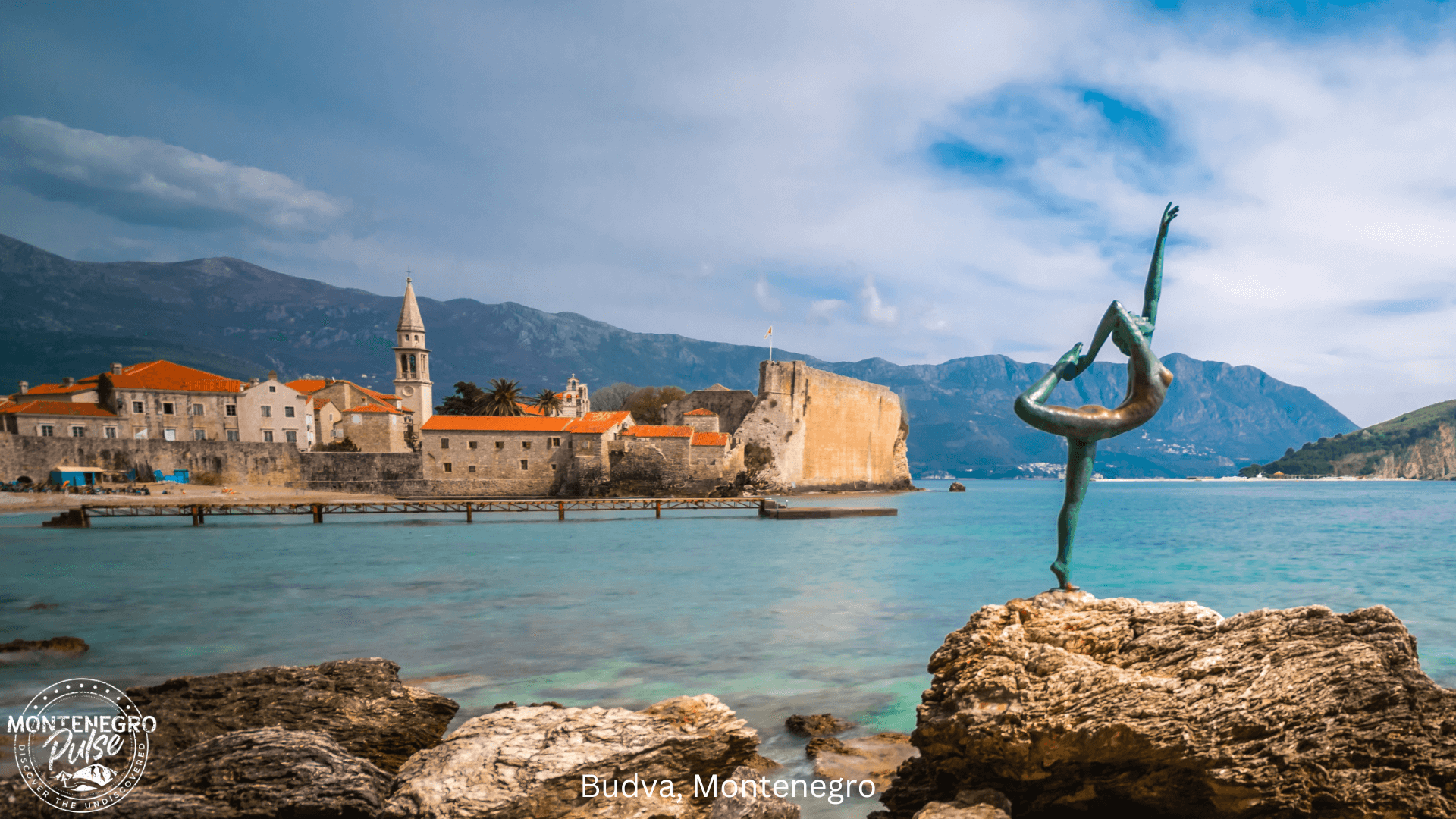 Statue of a dancer on a rock in front of the beach and historical Old Town of Budva, Montenegro.