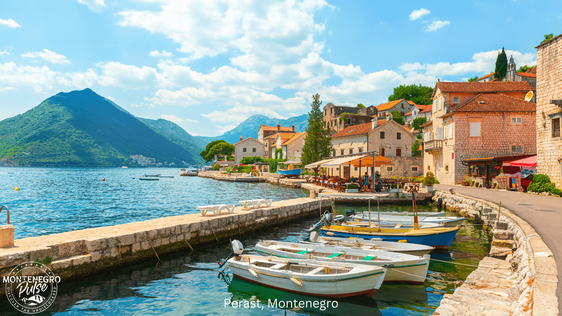Charming waterfront of Perast, Montenegro, with traditional stone houses and boats docked along the bay under a bright blue sky.