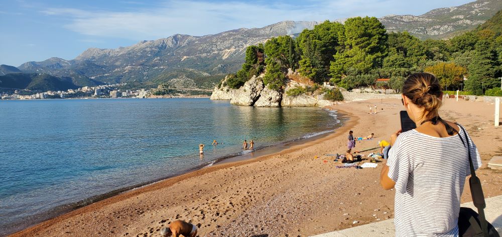 Sveti Stefan Beach During Autumn, Montenegro Tranquil Sveti Stefan beach scene with people enjoying warm sunshine against mountainous scenery during November in Montenegro.